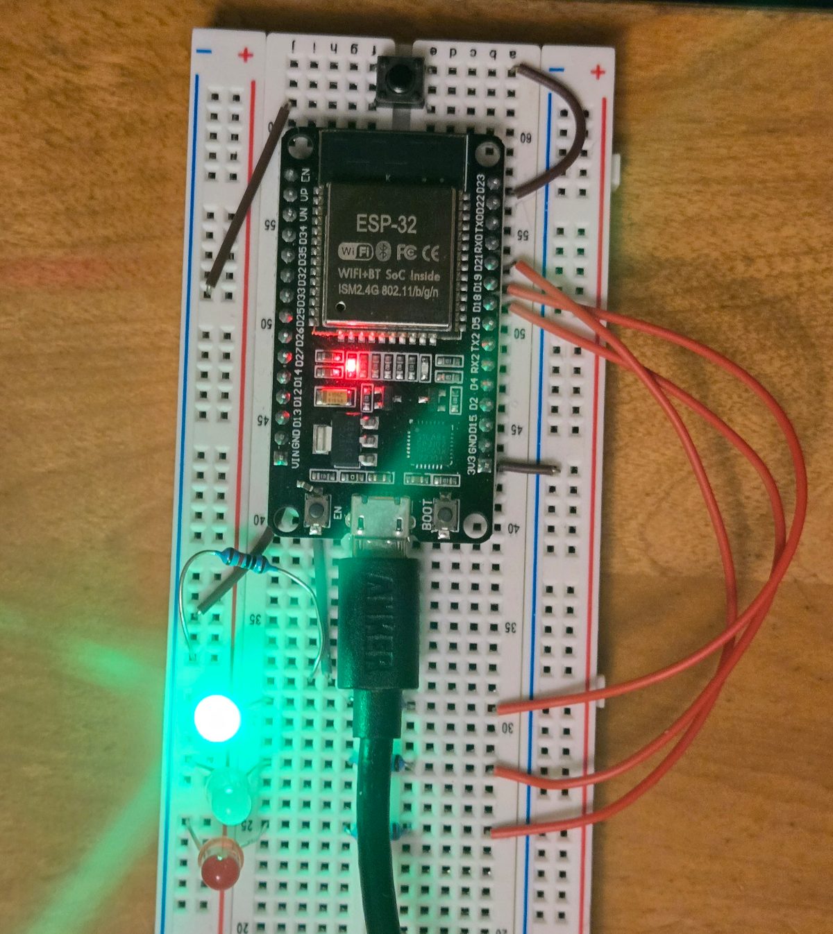 An ESP32 development board on a white breadboard, with jumper wires and three LEDs at the bottom left; one LED glows green.